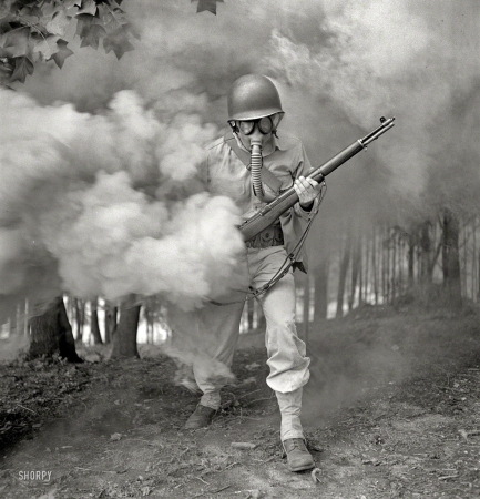 Photo showing: Smokescream -- September 1942. Fort Belvoir, Virginia. Sergeant George Camblair
learning how to use a gas mask in a practice smokescreen.