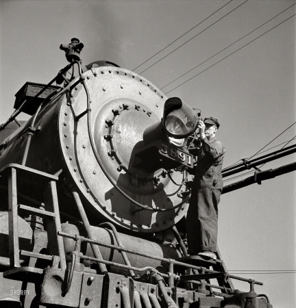 Photo showing: Light Cleaning -- March 1943. Needles, Calif. Electrician B. Fitzgerald cleaning the headlight of a locomotive at the Atchison, Topeka & Santa Fe yard.