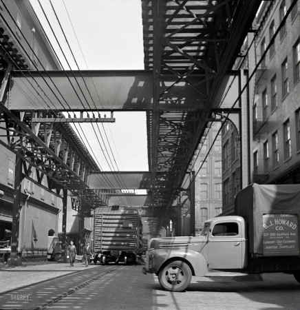 Photo showing: Inside Track -- April 1943. Baltimore, Maryland. Trucks and trains unloading goods underneath elevated trolley.