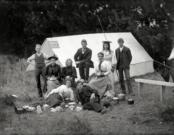 Photo showing: Clover Camp -- Circa 1905 near Christchurch, New Zealand. Young people with camping gear,
having tea and cake in front of tent with 'Clover Camp' sign.