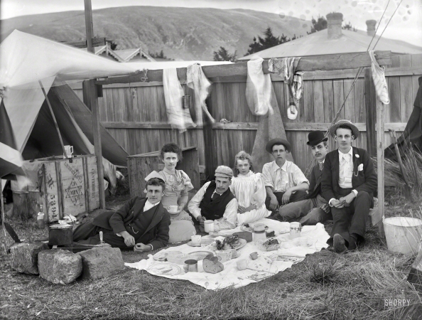 Photo showing: On the Ground -- New Zealand circa 1905. Unidentified group having a picnic outside tent in backyard of house, probably Christchurch district.