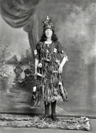 Photo showing: Be a Tree -- New Zealand circa 1910. Studio portrait, young woman in Christmas tree fancy dress
and hat costume, with little presents and decorations hanging off her, Christchurch.