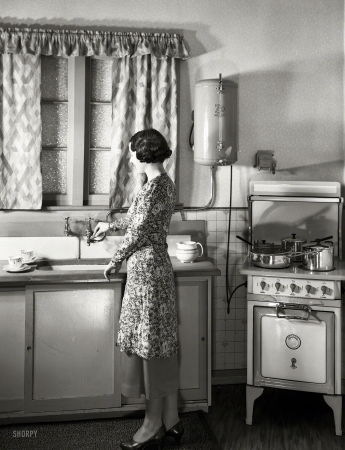 Photo showing: Dream Kitchen -- New Zealand circa 1930s. Model at sink in kitchen equipped with Atlas electric stove and Zip water heater.