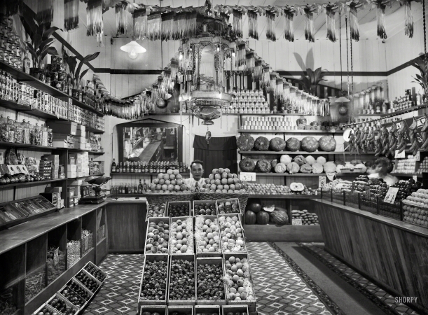 Photo showing: Apple Store -- Circa 1920s New Zealand. Greengrocery, probably Taranaki region. Chinese shopkeeper
with baskets of apples and boxes of peaches, cape gooseberries and other fruits. 